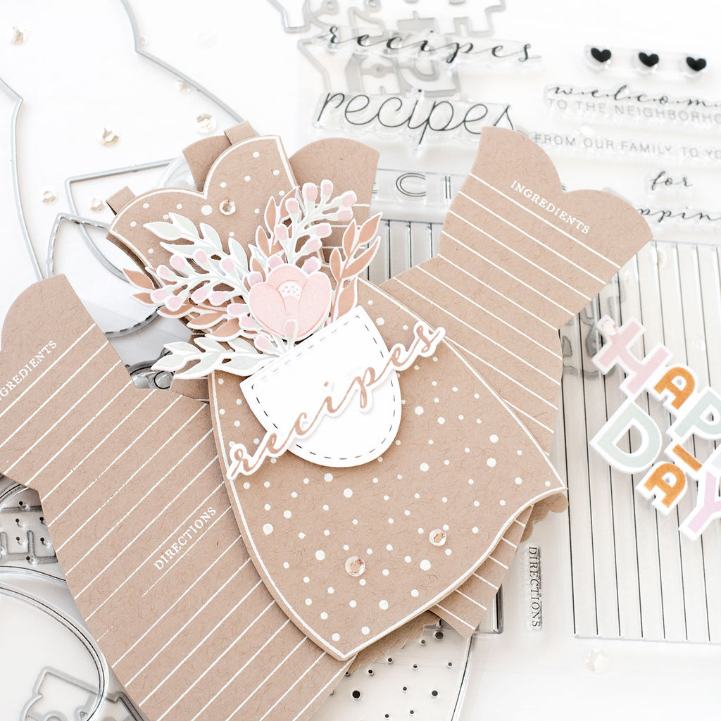 A recipe card rolodex, in the shape of our Apron Strings stamps and dies. The aprons are held together by the handy hinges, which are included in the Apron Strings die set. They allow the aprons to open up like a folding card, and for shaped recipe cards to be added inside.  The individual recipe cards are stamped with the Recipe Card builder stamp, to add lines and headings. The pocket of the apron is adorned with a bouquet of flowers from the Hello Beautiful Blooms stamp set.