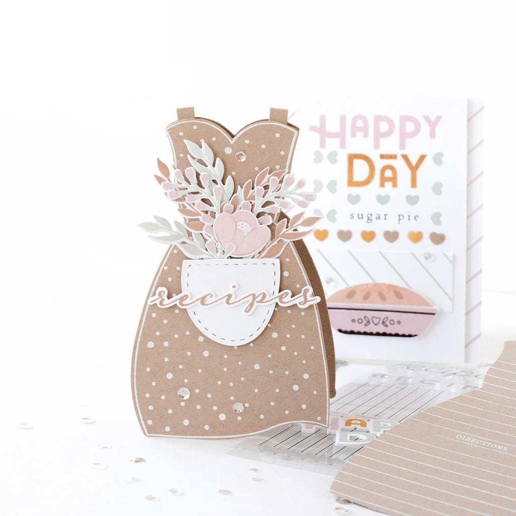 A recipe card rolodex, in the shape of our Apron Strings stamps and dies. The aprons are held together by the handy hinges, which are included in the Apron Strings die set. They allow the aprons to open up like a folding card, and for shaped recipe cards to be added inside. The pocket of the apron is adorned with a bouquet of flowers from the Hello Beautiful Blooms stamp set.