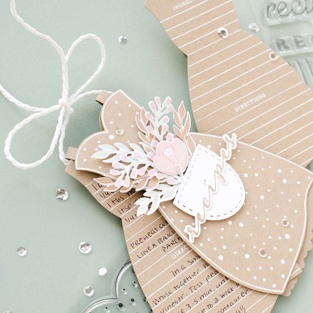 A close up image of the Apron Strings folding recipe card holder, which features the apron and individual apron recipe cards tucked inside.